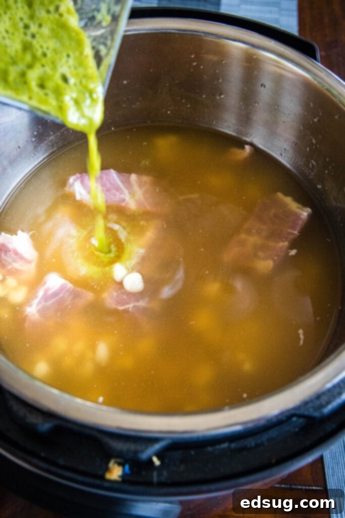 Effortless Instant Pot Pozole 5 pouring salsa verde into instant pot with pork and hominy, illustrating the recipe process