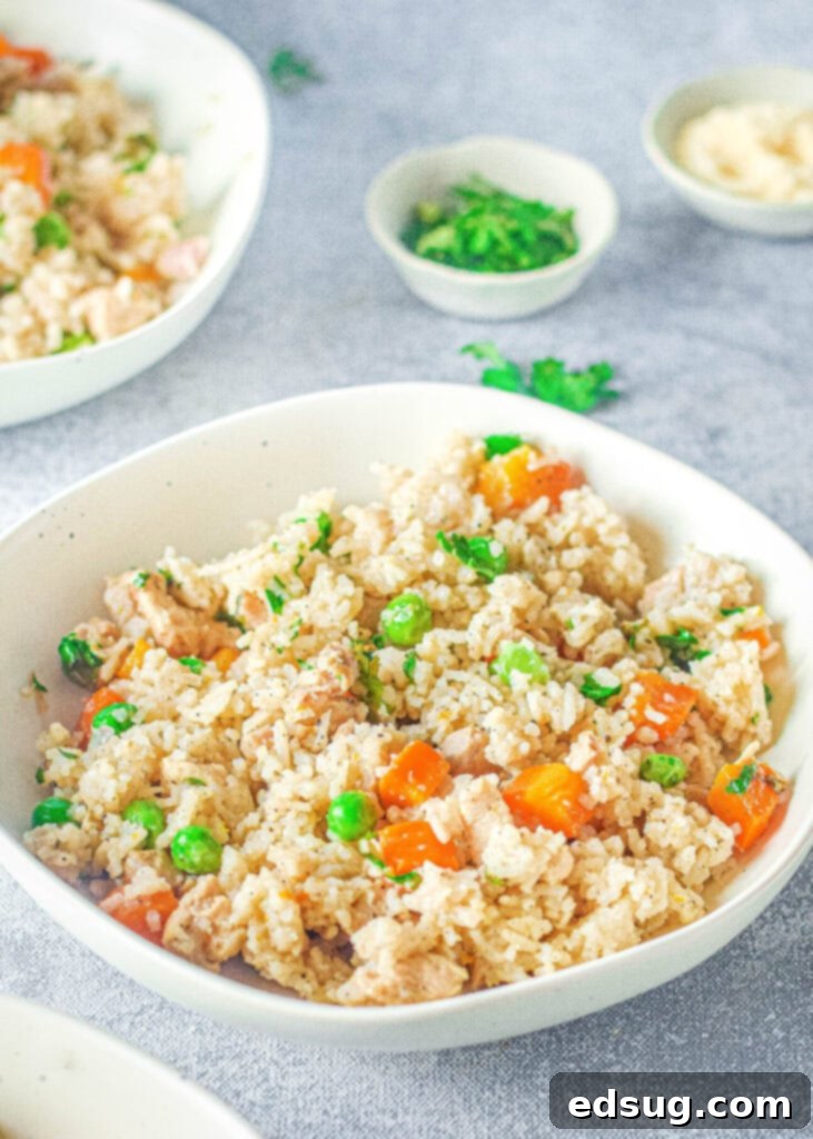 A close-up of fluffy, cooked white rice with vibrant green peas and tender carrots in a white bowl, highlighting its texture.