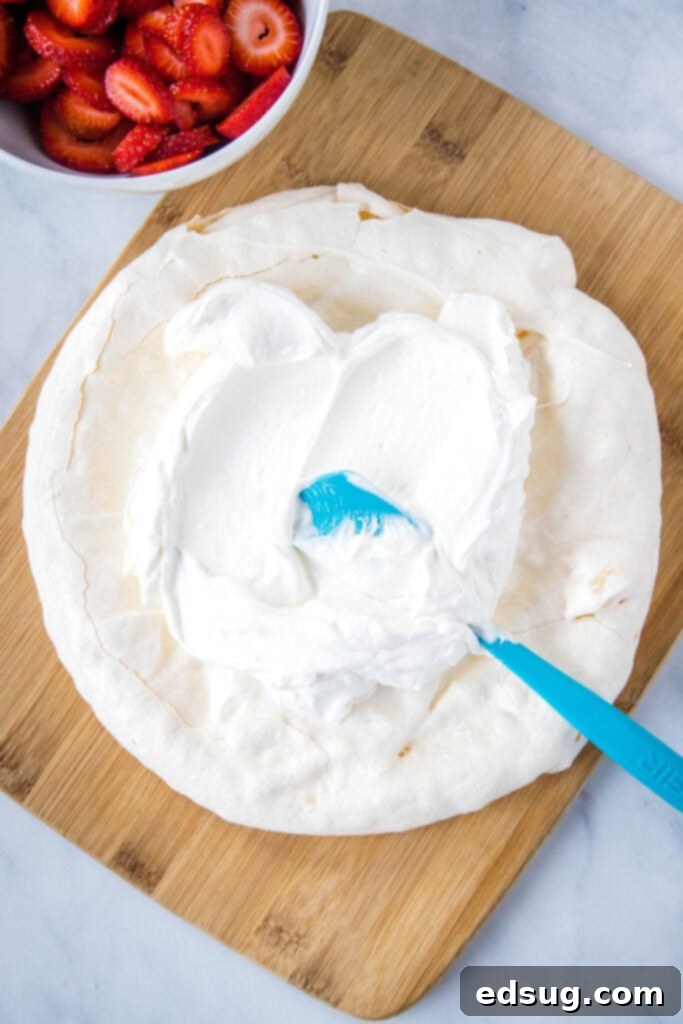 Perfect Pavlova 6 topping baked meringue with whipped cream and a bowl of strawberries near by