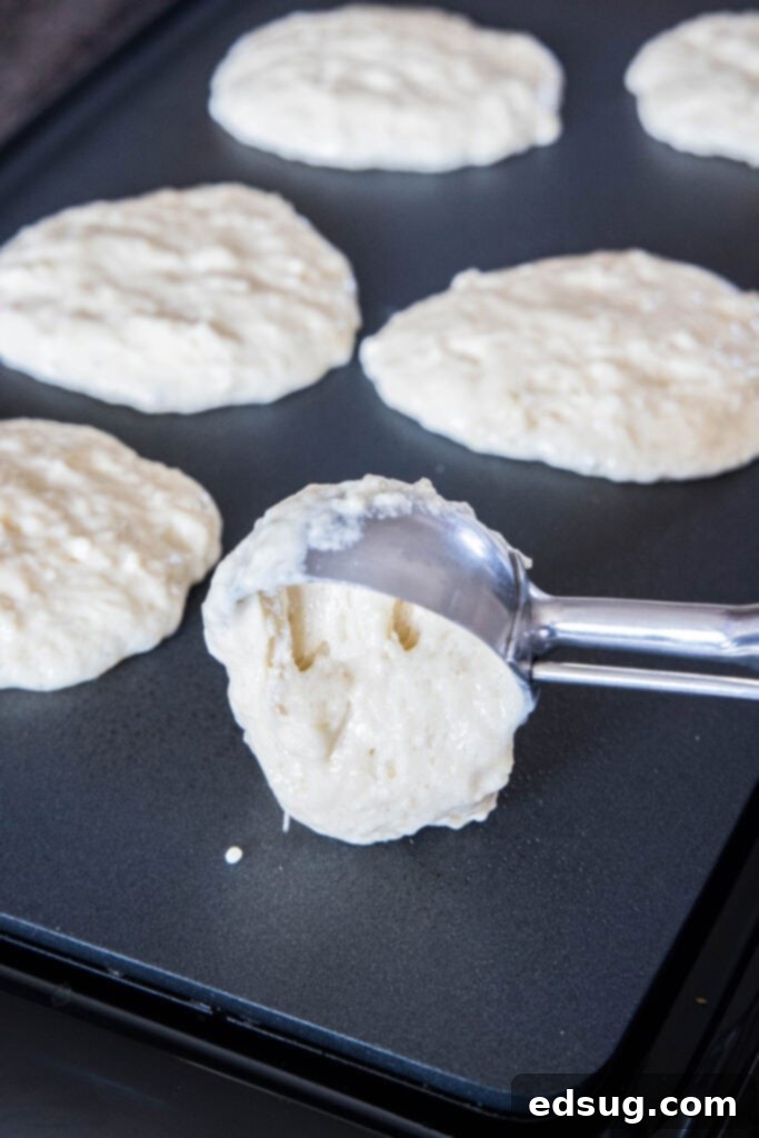 Hands scooping lemon pancake batter onto a hot griddle