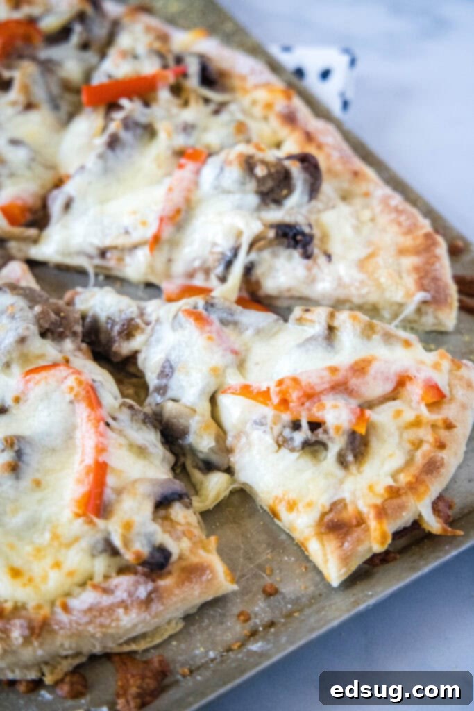 Philly Steakhouse Pizza 2 A delicious slice of Philly Cheesesteak Pizza on a baking tray, showcasing its golden crust and savory toppings.