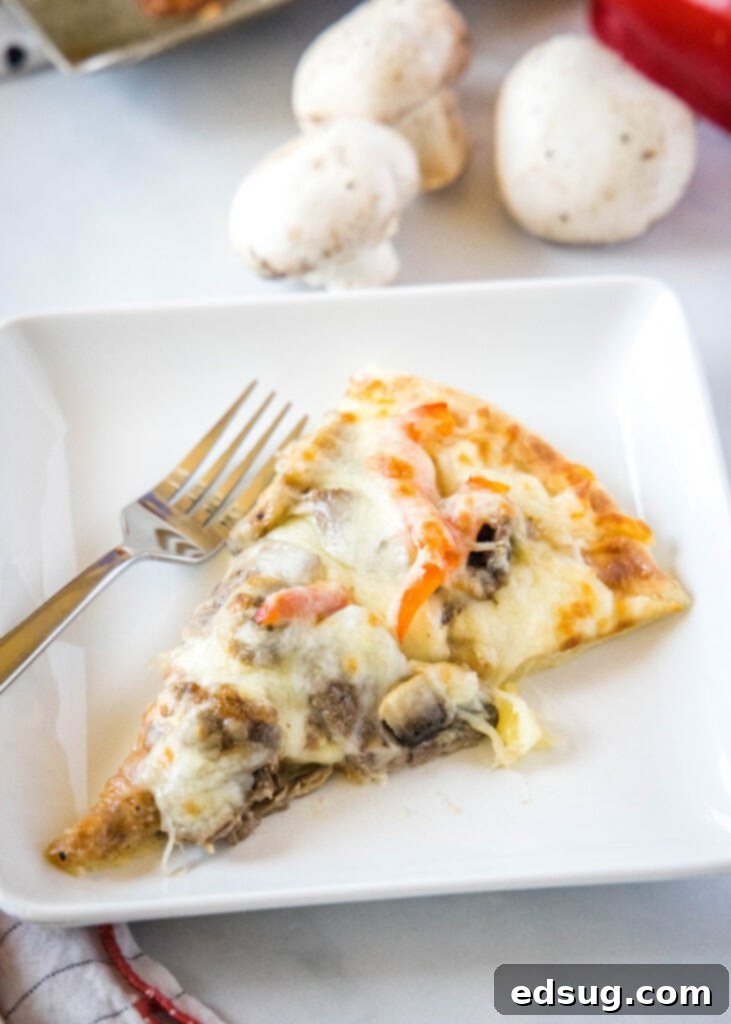 Philly Steakhouse Pizza 6 A single piece of freshly baked Philly Cheesesteak Pizza on a white plate, ready to be enjoyed.