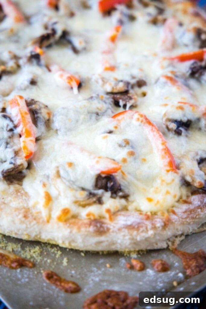 Philly Steakhouse Pizza 7 A full baked Philly Cheesesteak Pizza resting on a baking sheet, with visible melted cheese and savory toppings.