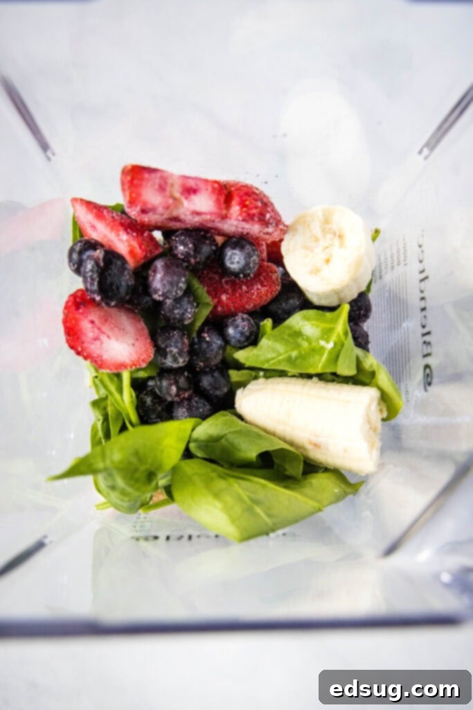 Berry Burst Smoothie 4 Fresh ingredients like mixed berries, banana, spinach, and yogurt being added to a blender for a smoothie