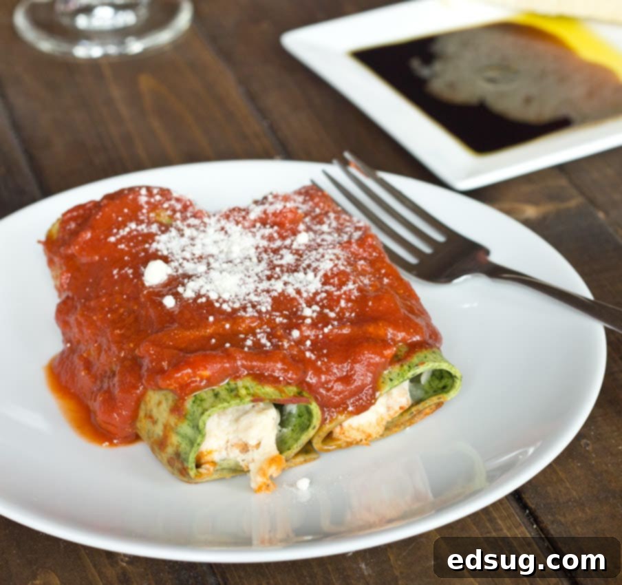 Portion of spinach pasta cannelloni on a plate, showing the creamy sausage and cheese filling inside.