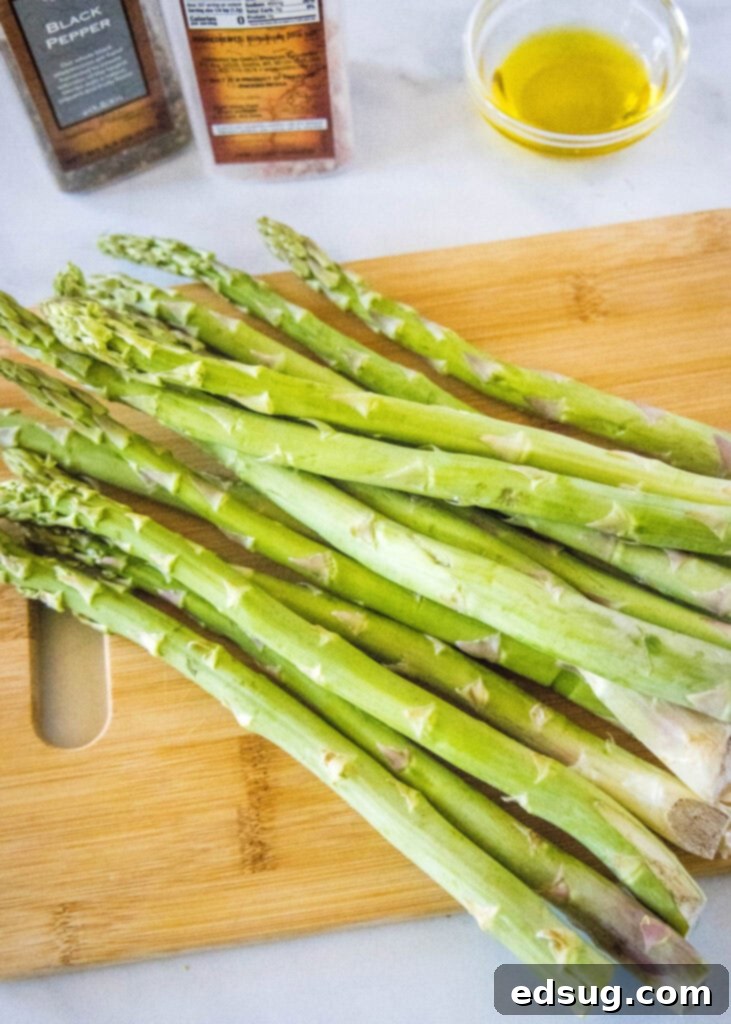 Ingredients for roasted asparagus laid out on a countertop, including fresh asparagus spears, a bottle of olive oil, salt, and pepper.