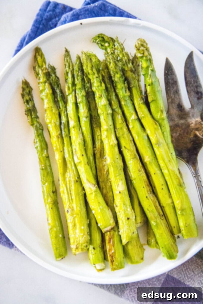 A serving of roasted asparagus on a white plate, with a serving fork, ready to be enjoyed as a healthy and delicious side.