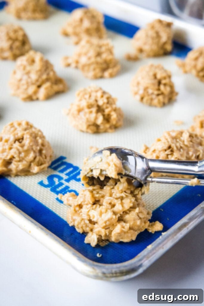 Scooping raw no-bake peanut butter cookie batter onto a lined baking sheet