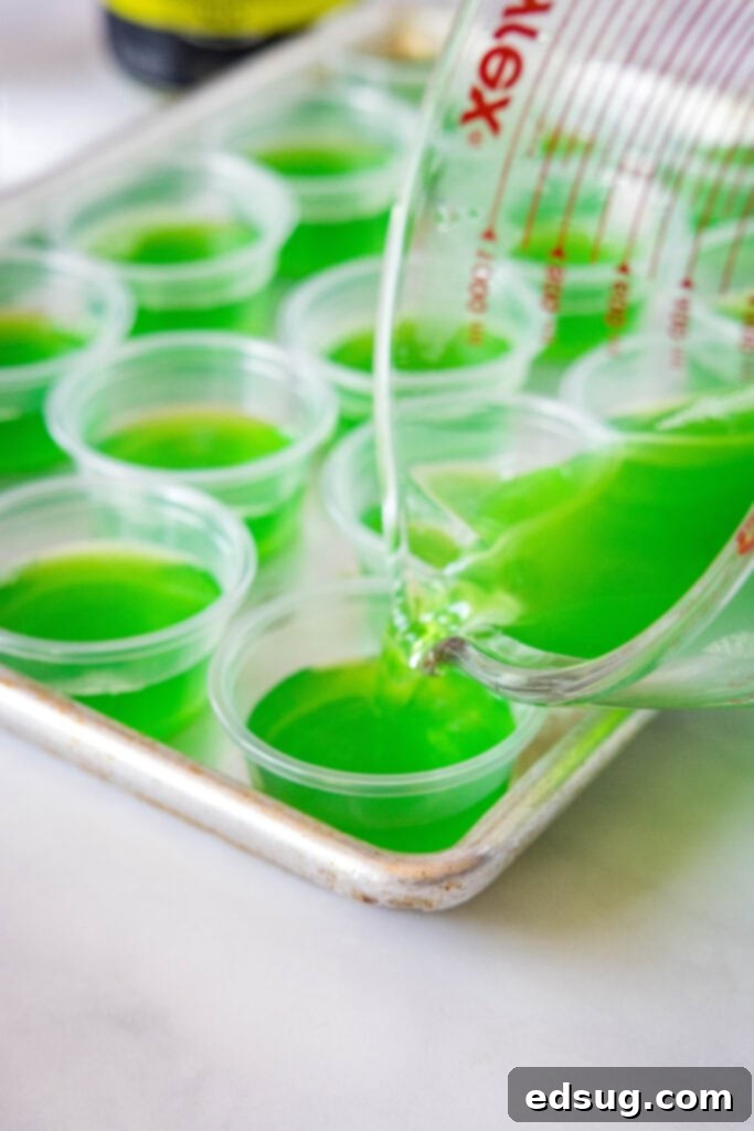 Tequila Lime Jiggle Shots 4 Pouring green margarita jello mixture into small plastic cups, demonstrating the preparation process