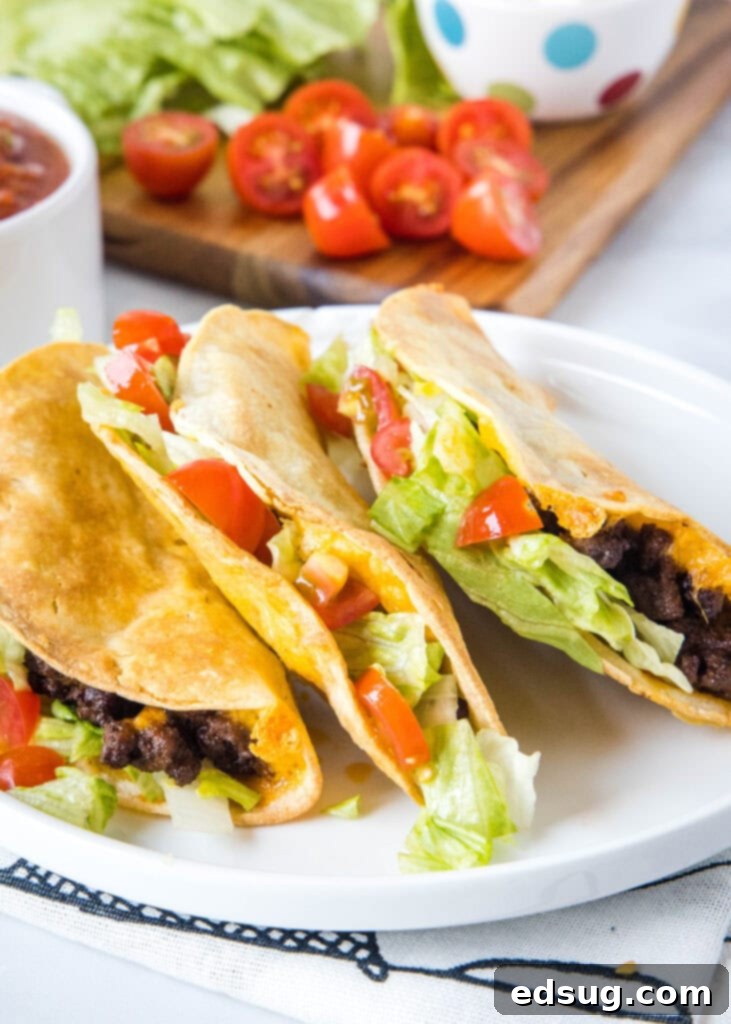 Crispy Air Fryer Tacos 2 A plate of golden-brown crispy tacos made in the air fryer, filled with seasoned ground beef, cheese, lettuce, and diced tomatoes, ready to be served.