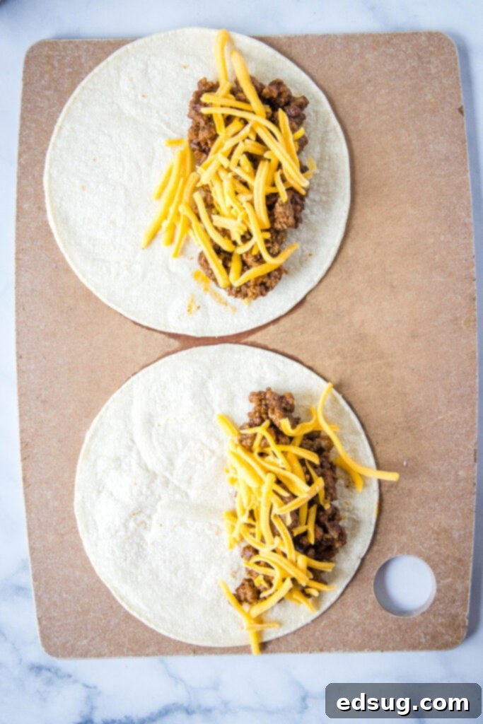 Crispy Air Fryer Tacos 3 Close-up view of corn tortillas being filled with savory seasoned ground beef and a generous sprinkle of shredded cheddar cheese before being folded.