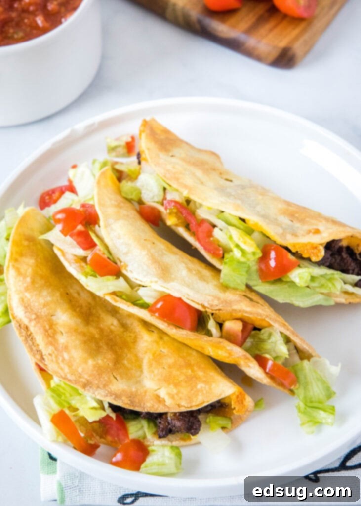 Crispy Air Fryer Tacos 5 A perfectly garnished plate of golden crispy air fryer tacos, topped with fresh lettuce, vibrant diced tomatoes, and a sprinkle of cheese.