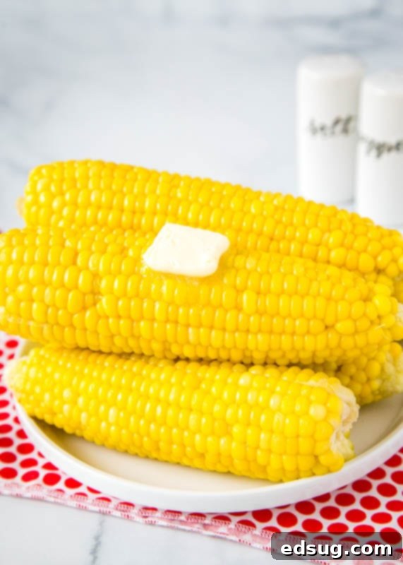 pressure cooker corn on the cob stacked on a white plate with pat of butter on top