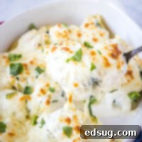 close up scooping alfredo stuffed shells out of baking dish