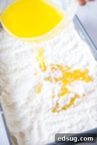 Drizzling melted butter over the dry cake mix and pecan layer in the baking dish.