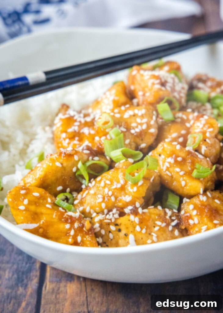 A close-up of finished Bourbon Chicken in a white bowl, showing the thick, glossy sauce