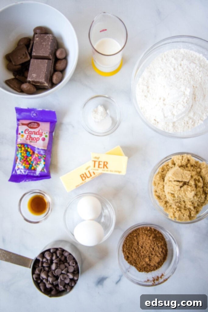 Stellar Brownie Cookies 3 Ingredients for cosmic brownie cookies laid out on a kitchen counter: butter, brown sugar, cocoa powder, milk chocolate, eggs, vanilla extract, baking powder, salt, semi-sweet chocolate chips, heavy cream, and rainbow chips.