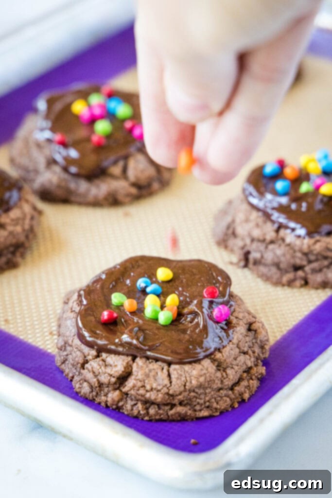 Stellar Brownie Cookies 4 Close-up of hands sprinkling colorful rainbow chips onto freshly ganached cosmic brownie cookies on a baking sheet, creating the signature look.