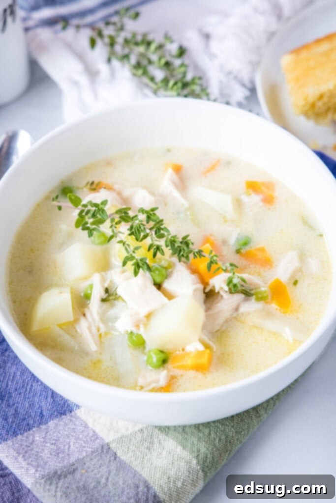 Creamy Chicken Pot Pie Soup 2 A white bowl of creamy chicken pot pie soup garnished with a sprig of fresh thyme on top, ready to be enjoyed.