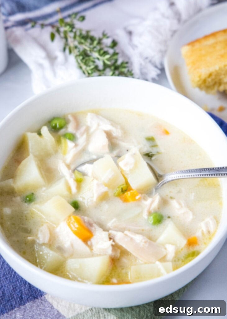 Creamy Chicken Pot Pie Soup 5 A wooden spoon scooping creamy chicken pot pie soup from a white bowl, showing the rich texture and visible pieces of chicken and vegetables.