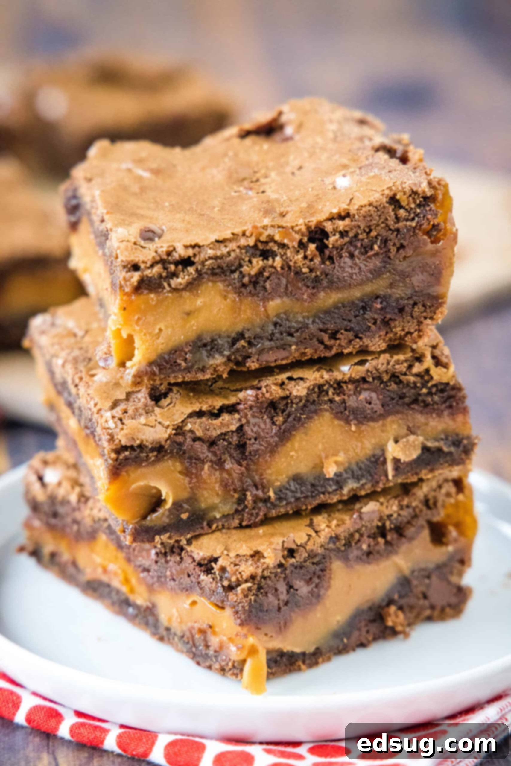 Experience the ultimate decadence with our rich, fudgy salted caramel brownies, featuring a luscious, melty caramel filling. Three perfectly stacked salted caramel brownies on a white plate, showcasing their fudgy texture and caramel layer.