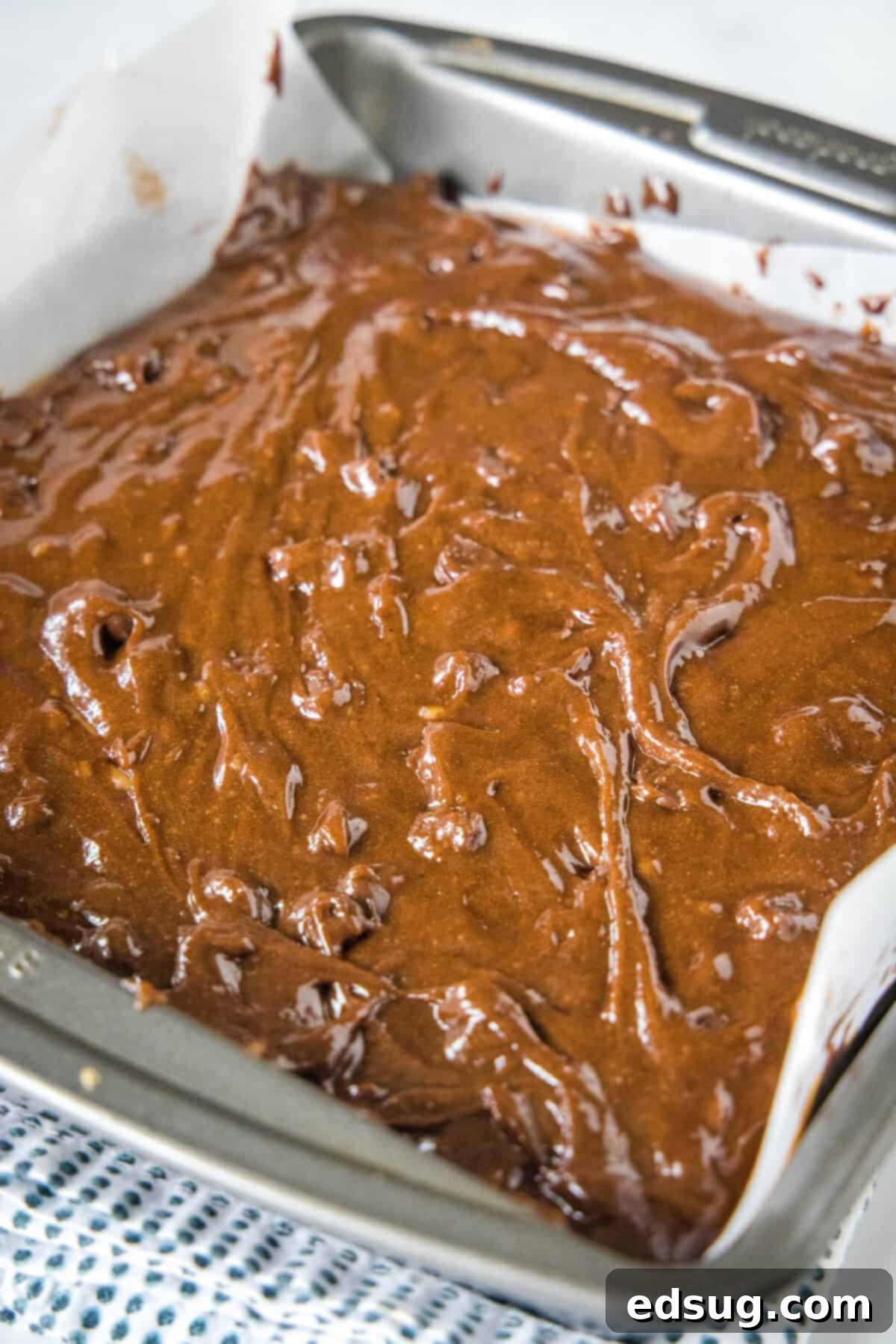 The final step before baking: dollop remaining brownie batter over the caramel layer and prepare for the oven. The final layer of chocolate brownie batter carefully dolloped over the salted caramel, creating an enticing marbling effect before baking.