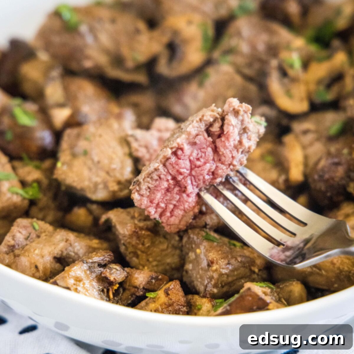 A piece of steak on a fork with a plate of steak and mushroom bites in the background