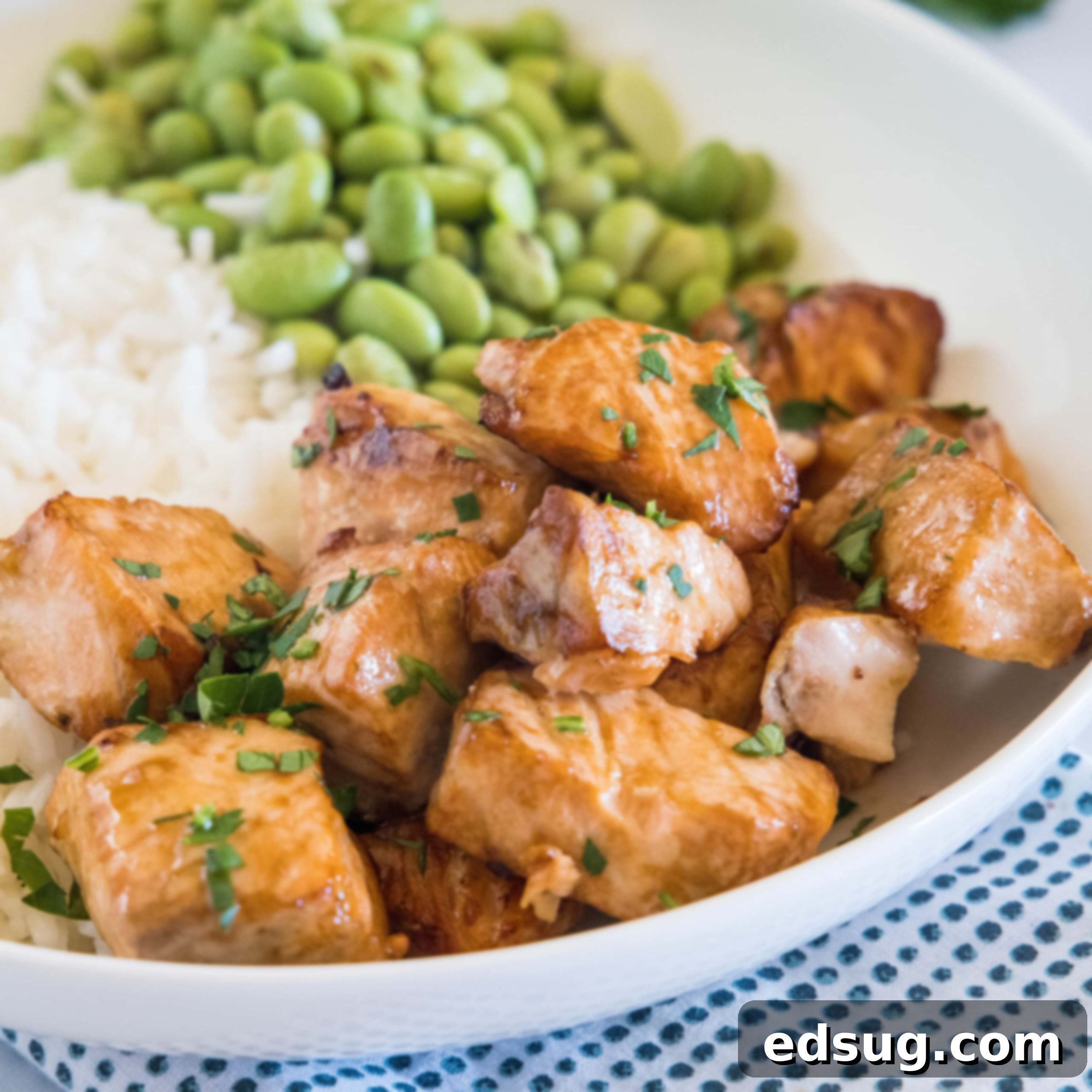Salmon bites served with rice and edamame beans in a white bowl.