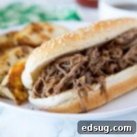 Melt-in-Your-Mouth Slow Cooker French Dip Sandwiches 2 A close up of a French dip sandwich on a plate with dipping au jus.