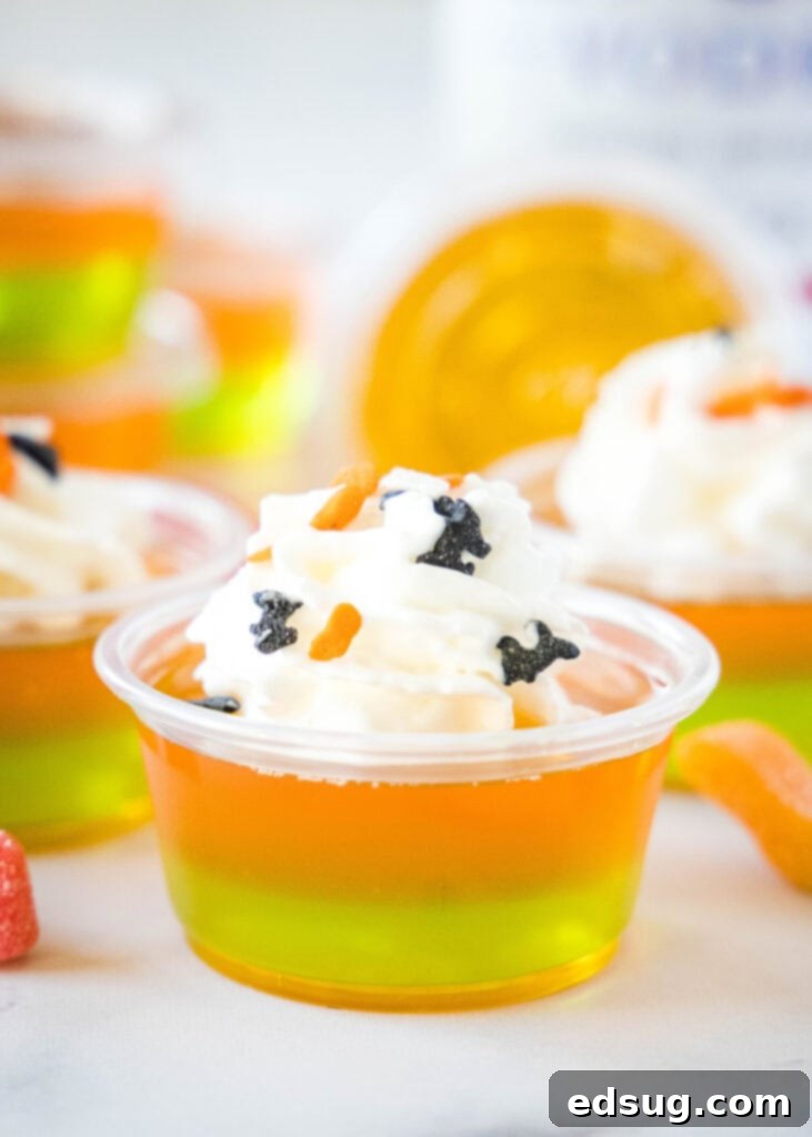 Witches Brew Jello Shots 2 Vibrant orange and green Halloween Jello Shots topped with fluffy whipped cream and festive sprinkles, ready for a party.