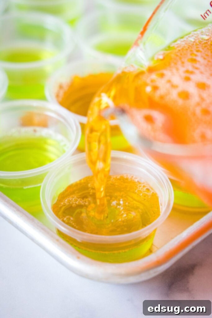 Witches Brew Jello Shots 4 Pouring the orange Jell-O mixture over the set green layer in small plastic cups, carefully creating a two-toned Halloween Jello Shot.