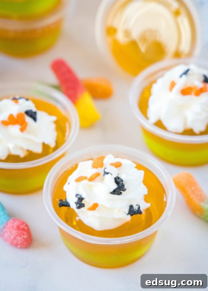 Witches Brew Jello Shots 6 Close-up view of perfectly layered orange and green Halloween Jello Shots, topped with rich whipped cream, awaiting a party.
