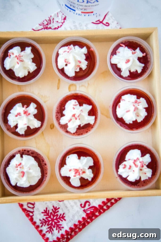 Merry & Bright Jello Shots 7 Overhead view of a tray filled with multiple festive Christmas JELL-O shots, garnished with whipped cream and sprinkles, perfect for a holiday gathering.