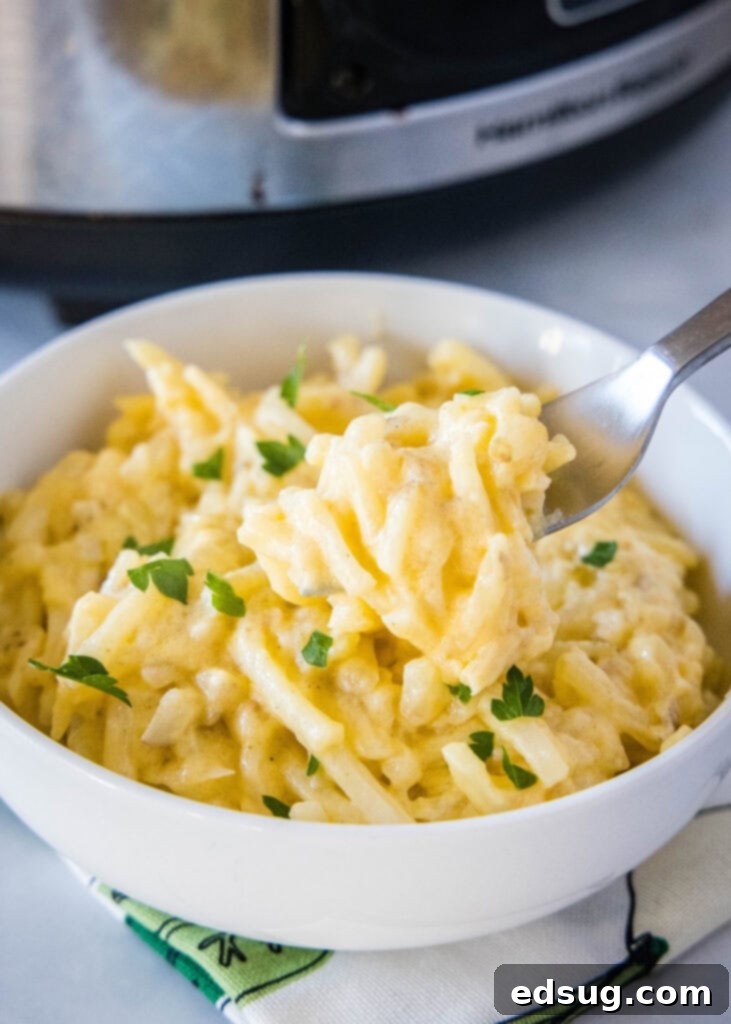 Easy Crockpot Cheesy Hashbrown Bake 2 A forkful of golden, cheesy hashbrown casserole being lifted from the dish, showing its creamy texture and melted cheese.
