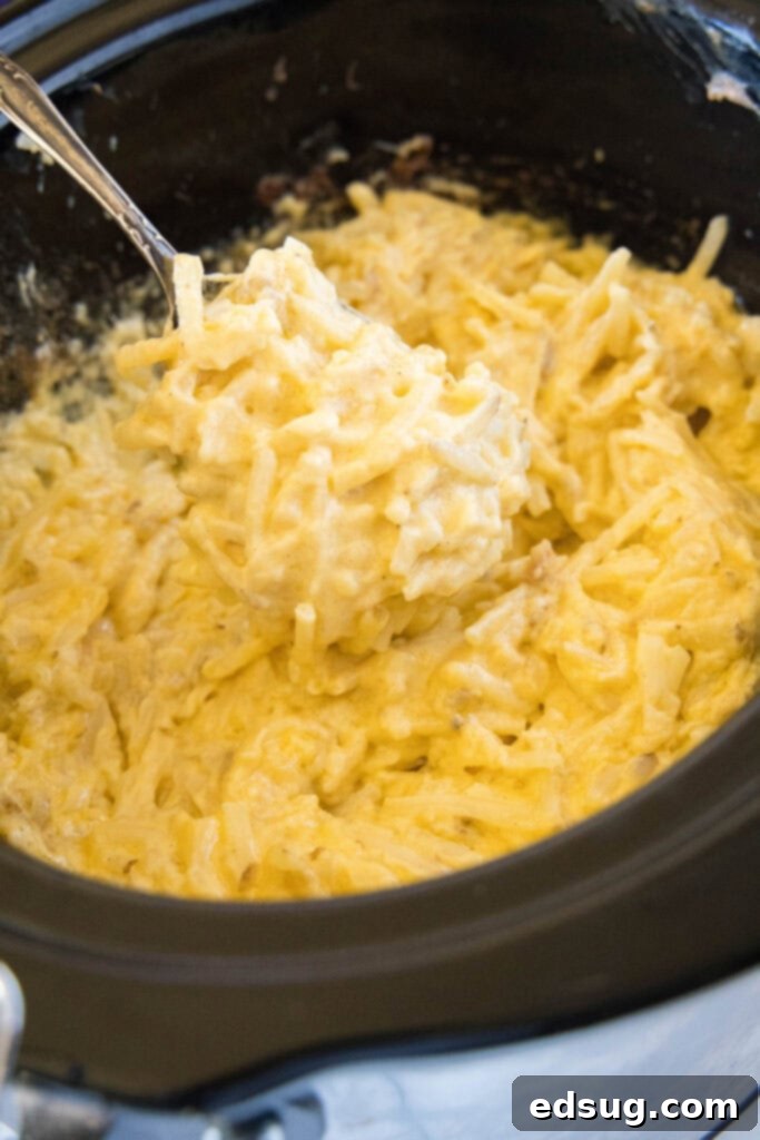 Easy Crockpot Cheesy Hashbrown Bake 4 Scooping out a generous portion of cheesy hashbrown casserole directly from the crockpot, steaming hot and ready to eat.