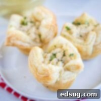 close up 3 crab puffs on a white plate, showcasing their flaky pastry and golden finish