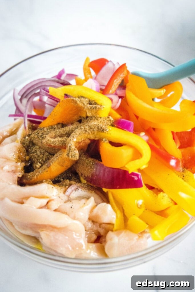 Thinly sliced chicken, onions, and bell peppers tossed with fajita seasoning in a mixing bowl.