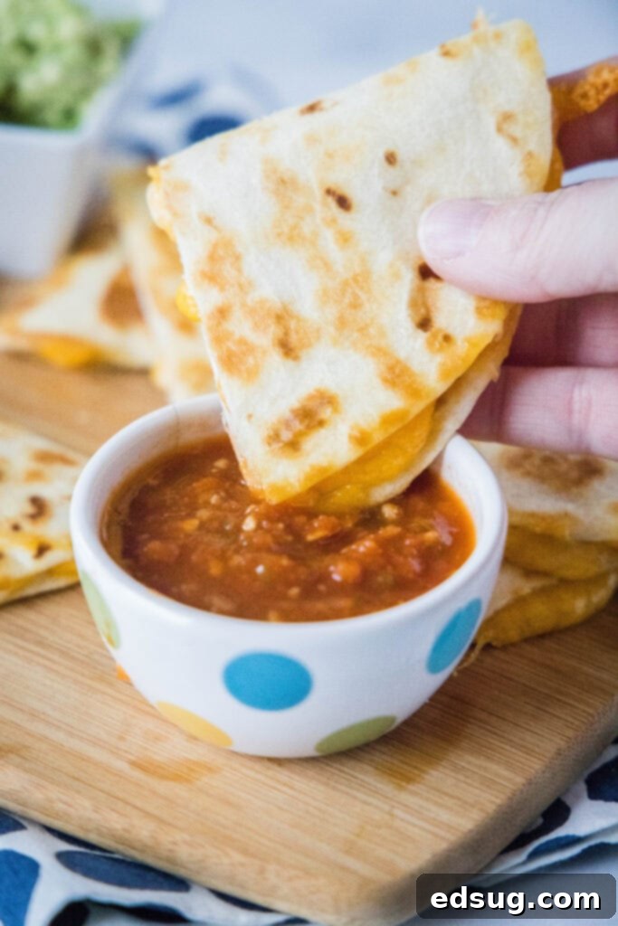 Melty Cheese Quesadilla 6 A hand dipping a crispy cheese quesadilla triangle into a bowl of fresh salsa.