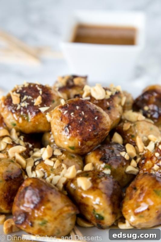 A plate of golden-brown chicken meatballs coated in peanut sauce, garnished with fresh cilantro and chopped peanuts, ready to be served.