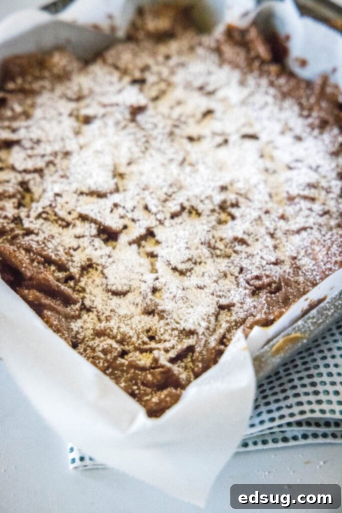 Snow-Dusted Chocolate Peanut Butter Bars 5 Fudgy Puppy Chow Bars neatly arranged in a baking pan, completely dusted with powdered sugar, signifying they are fully prepared and ready for slicing.