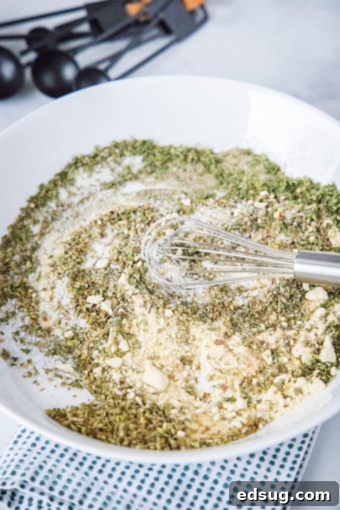 Classic Italian Salad Mix 3 Dried spices being carefully mixed together on a white plate with a spoon, illustrating the preparation of homemade Italian dressing mix.