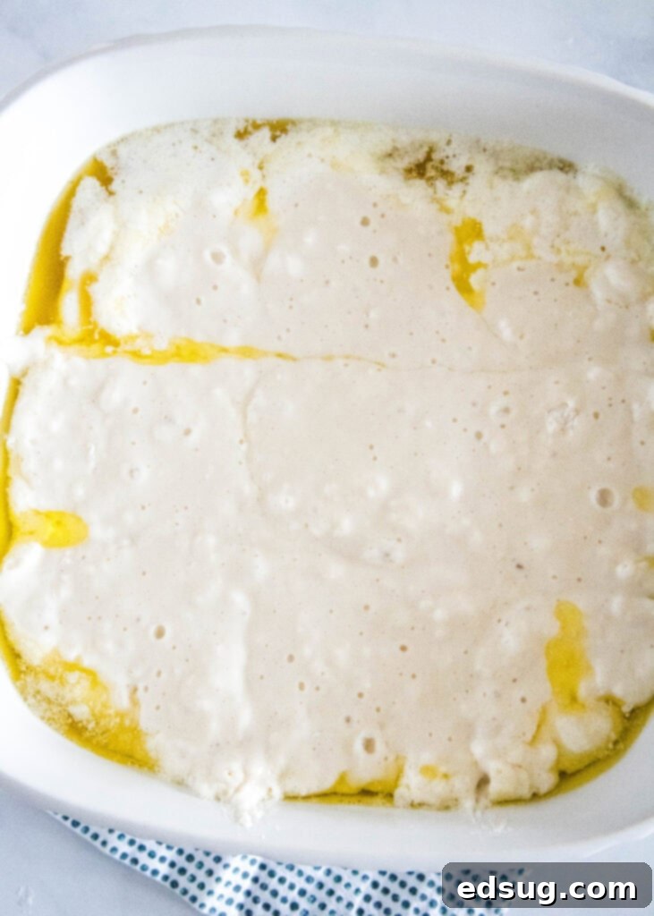 The simple biscuit dough, light and creamy, poured into an 8-inch baking dish already containing a shimmering pool of melted butter, ready for its transformation in the oven.