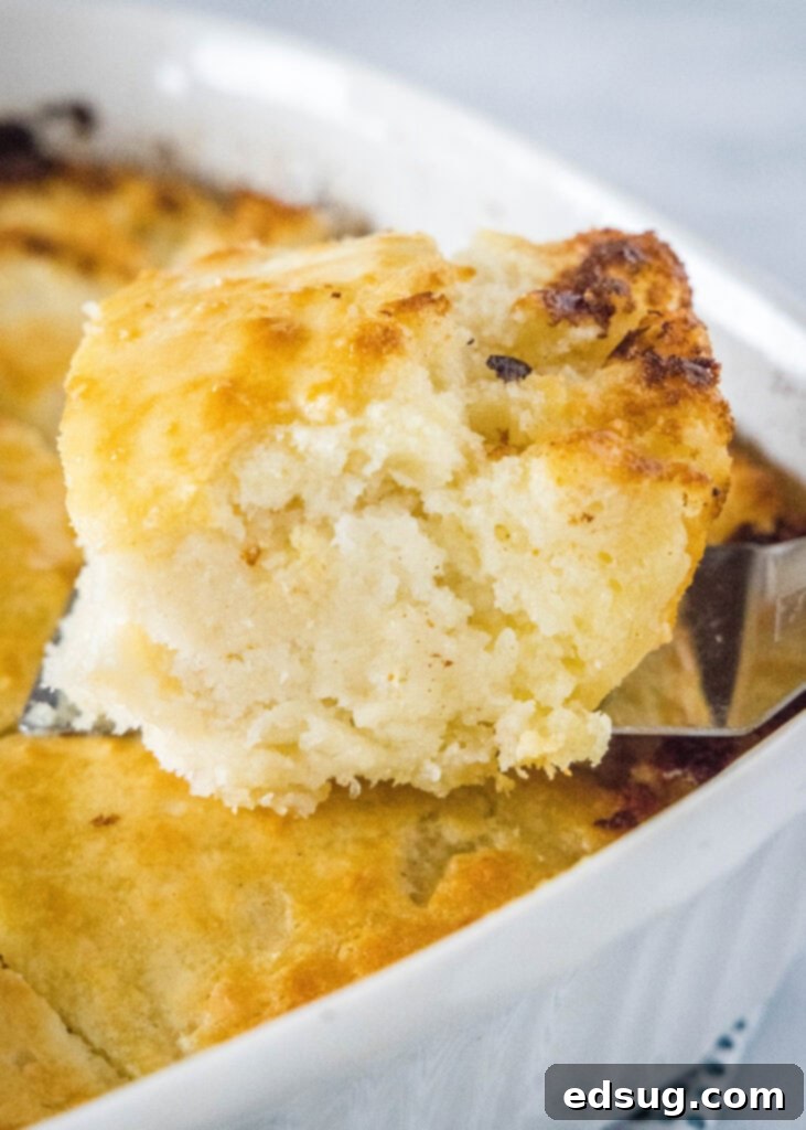 A golden-brown butter swim biscuit being lifted from the baking pan with a spatula, revealing its tender underside and the remaining buttery goodness in the pan.
