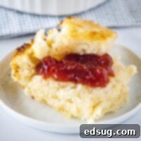 A soft butter swim biscuit with a dollop of mixed berry jam on top, presented on a round white plate, ready to be enjoyed.