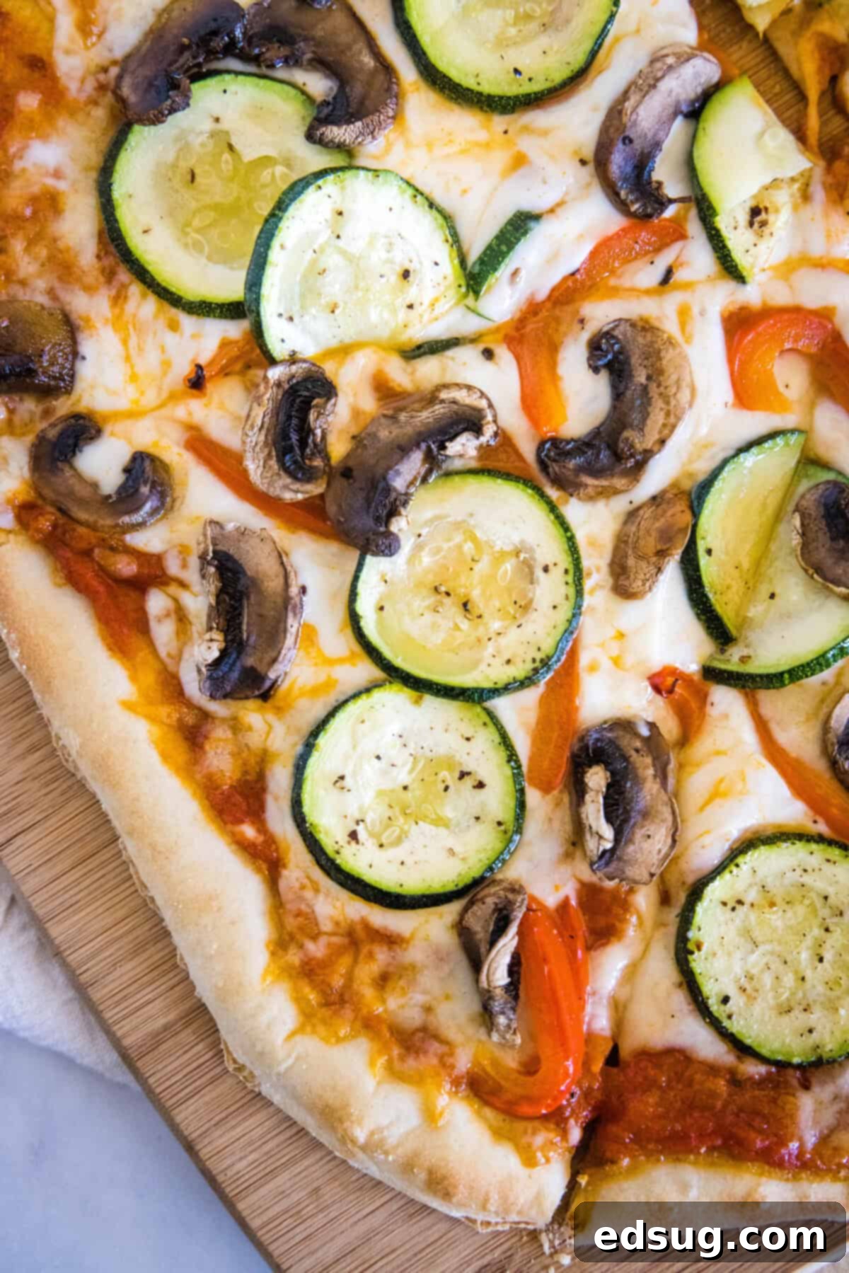 Roasted Veggie Pizza | Dinners, Dishes, and Desserts Sliced homemade roasted veggie pizza on a wooden cutting board, showcasing its golden crust and colorful toppings.