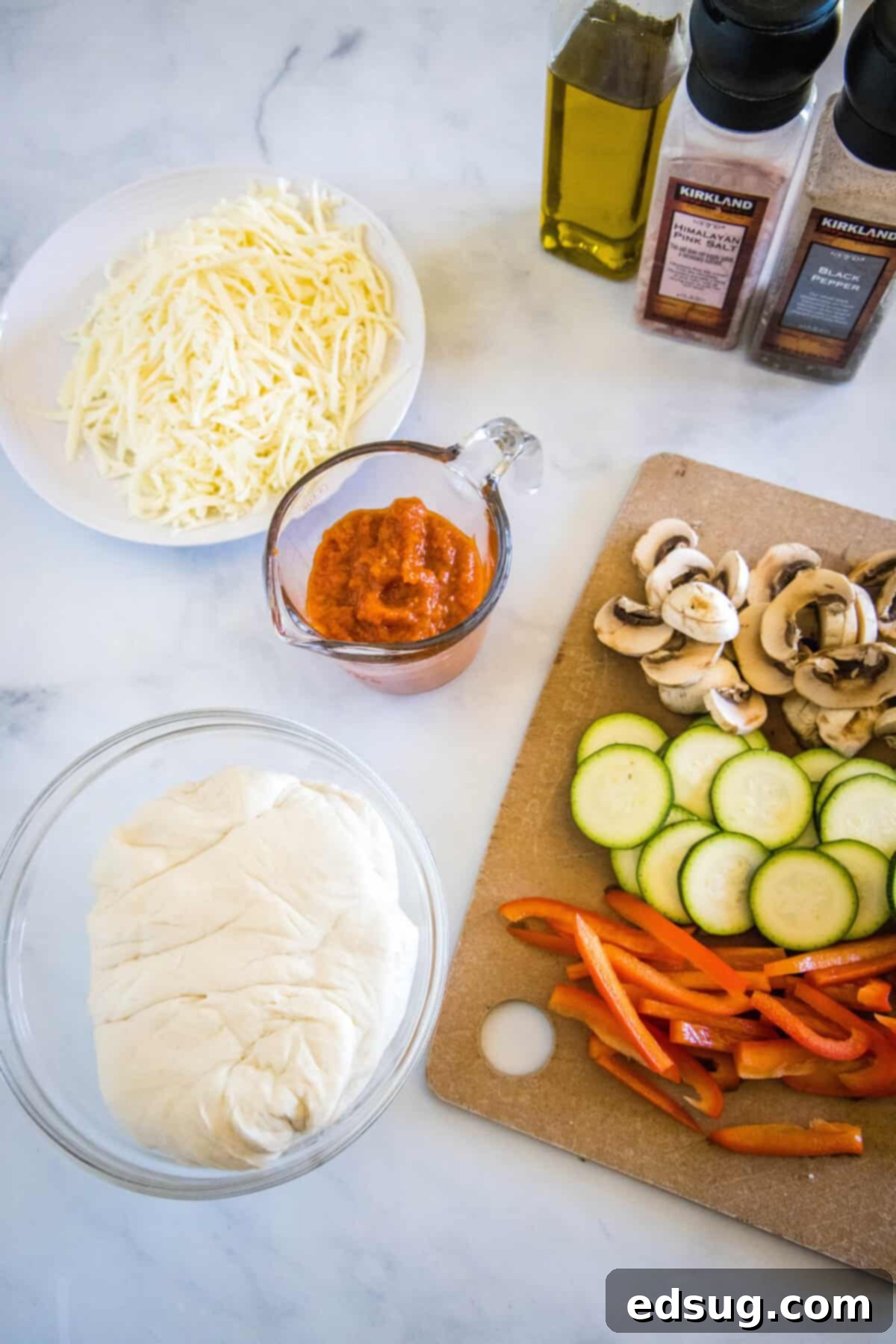Roasted Veggie Pizza Fresh ingredients laid out for making roasted veggie pizza, including zucchini, mushrooms, bell peppers, mozzarella, sauce, and dough.