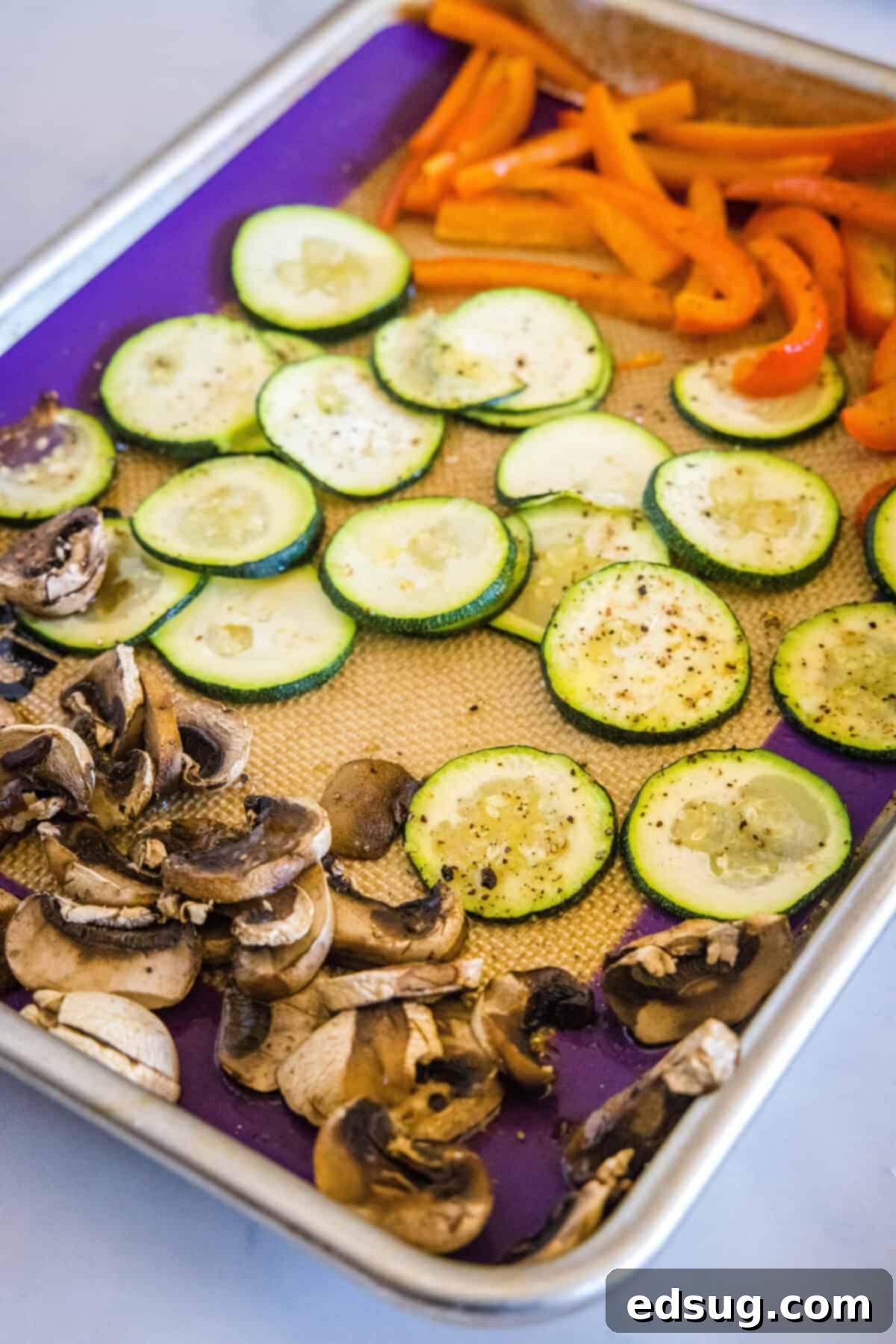 Gourmet Roasted Vegetable Pizza 2 Sliced zucchini, mushrooms, and bell peppers seasoned with olive oil, salt, and pepper on a baking sheet, ready for roasting.