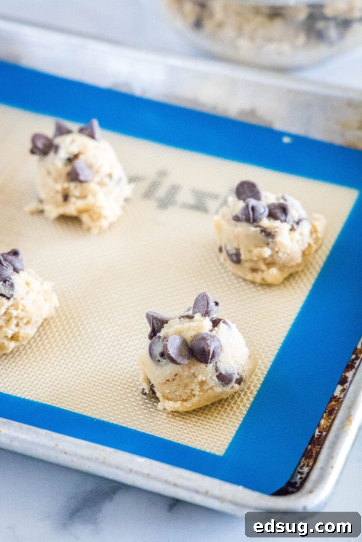Raw chocolate chip cookie dough balls on a silicone mat on a baking sheet