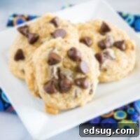 Three chocolate chip cookies on a white square plate, on top of a kitchen towel