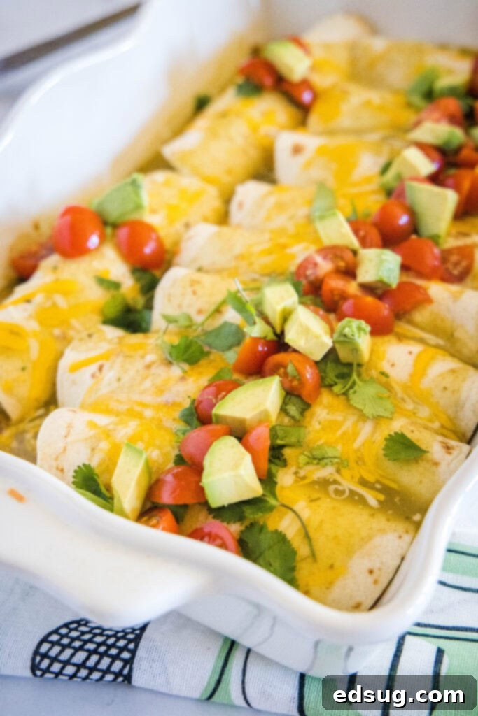 Ultimate Breakfast Enchiladas 2 breakfast enchiladas topped with avocado, and tomatoes in a baking dish